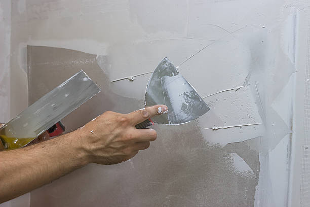 man hand with trowel plastering a wall, skim coating plaster walls